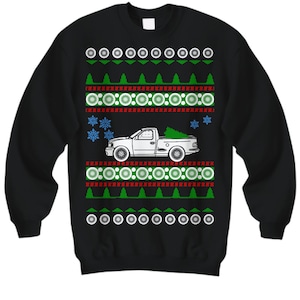 Puede incluir: Suéter navideño negro con una camioneta blanca que lleva un árbol de Navidad. El suéter tiene un patrón rojo, blanco y verde con copos de nieve.