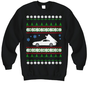 Könnte beinhalten: Schwarzer Weihnachtspullover mit einem weißen Auto, das einen Weihnachtsbaum transportiert. Der Pullover hat ein sich wiederholendes Muster aus Schneeflocken, grünen Bäumen und roten und weißen Kreisen.