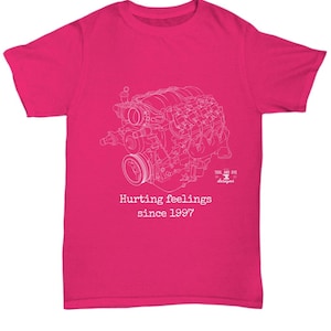Puede incluir: Una camiseta magenta con un dibujo lineal blanco de un motor. El texto "Hurting feelings since 1997" está impreso debajo del gráfico del motor. La camiseta tiene cuello redondo y mangas cortas.