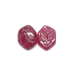 May include: Two faceted, hexagonal, ruby-coloured gemstones. Each gem features a carved leaf design. The gems are set against a white background, highlighting their rich colour and intricate details. Ideal for jewellery making.
