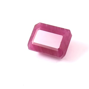 Może przedstawiać: Fasetowany, prostokątny kamień szlachetny rubinu w odcieniu różu. Klejnot ma dużą, prostokątną fasetę środkową i fazowane krawędzie. Kamień szlachetny jest umieszczony na białym tle.