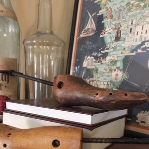 May include: Two wooden shoe stretchers, one brown and one light brown, are on a wooden surface. The brown shoe stretcher is on top of a book with a brown cover. The book is on a wooden surface.