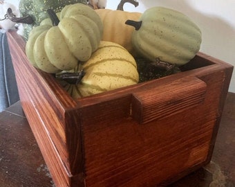 May include: A wooden box with a handle, filled with decorative gourds in shades of green and yellow. The box is stained a rich brown color.