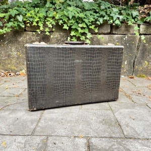 May include: A vintage brown suitcase with a crocodile-embossed pattern. The suitcase has a metal handle and a latch.