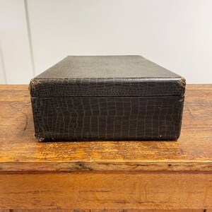 May include: A dark brown leather box with a crocodile-embossed pattern. The box is sitting on a wooden surface.