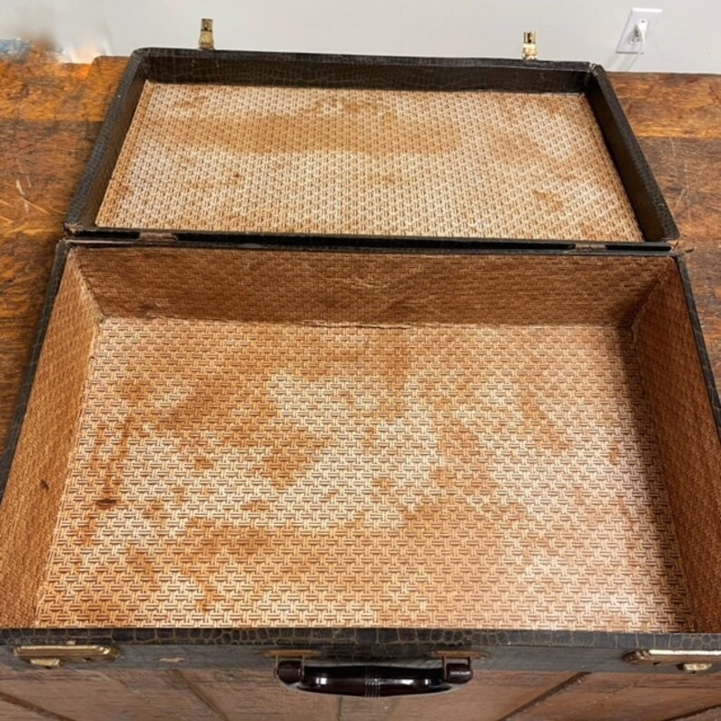 May include: An open vintage brown leather suitcase with a woven brown fabric lining. The suitcase has a black handle and brass hardware.