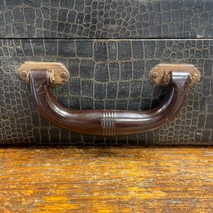 May include: A black vintage suitcase with a crocodile-embossed leather exterior and a brown plastic handle.