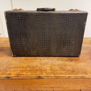 May include: A vintage brown leather suitcase with a crocodile pattern. The suitcase has a black handle and is closed.