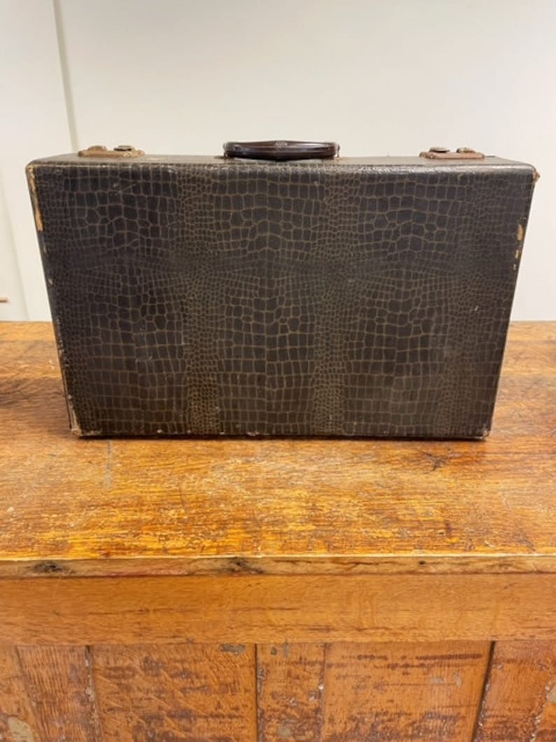 May include: A vintage brown leather suitcase with a crocodile pattern. The suitcase has a black handle and is closed.
