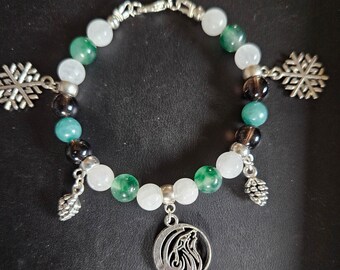 May include: A silver bracelet with white, green, and black beads. The bracelet has two snowflake charms and a wolf charm.