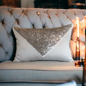May include: A light gray tufted sofa with a decorative throw pillow featuring a silver sequin triangle design.