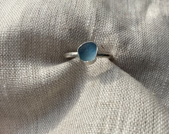 May include: A silver ring with a light blue stone set in the center. The stone is irregularly shaped and has a smooth, polished surface.
