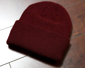 May include: A burgundy knitted beanie hat. The hat is made of a soft, warm material and has a simple, classic design.