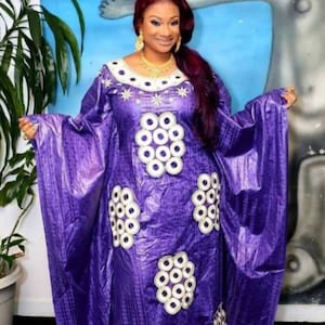 May include: A purple dress with white embroidery. The dress has a long, flowing skirt and a high neckline. The embroidery is in the shape of circles and stars.