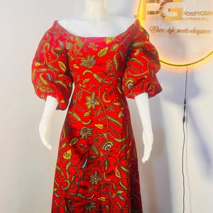 May include: A red maxi dress with a floral print and off-the-shoulder neckline. The dress has large, puffy sleeves and a flowing skirt. The dress is on a white mannequin.