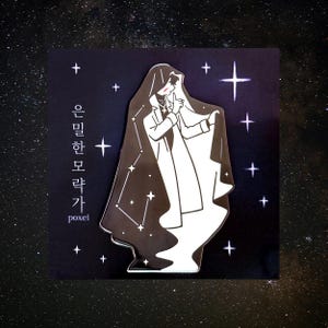May include: A black and white enamel pin featuring a figure in a hooded cloak with a constellation design. The pin has the text "은밀한 모략가" and "poxei" in Korean. The background is a dark blue with white stars.