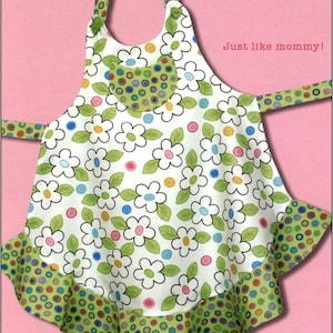 May include: A green and white child's apron with a floral print and a pocket. The apron has a ruffled bottom and is trimmed with green and white polka dots. The text "Child's Apron" and "Just like mommy!" is printed on the apron. The apron is available in three sizes: small, medium, and large.