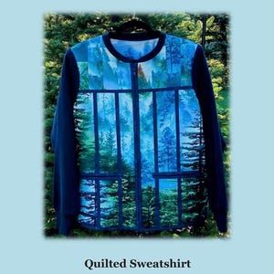 May include: A quilted sweatshirt jacket featuring a forest landscape print with blue and green tones, a full-length front zipper, and solid dark blue sleeves. The text "Playing with Panels", "Quilted Sweatshirt Jacket", and "JMD201" is visible.