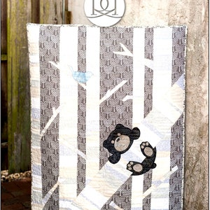 May include: A quilt with a white and gray background featuring a black bear and a blue bird. The quilt is titled "TIMBER!" and is designed by RACHEL ROSSI.