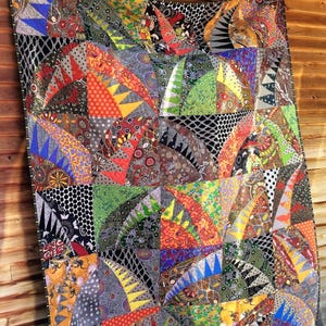 May include: A quilt featuring a complex patchwork design of semicircular fan shapes. The fabric panels display a variety of vibrant colors including orange, green, blue, and yellow, combined with intricate black and white geometric patterns.