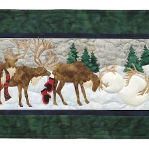 May include: A quilted Christmas table runner featuring a winter scene with brown reindeer, snowballs, and evergreen trees. The reindeer wear a Santa hat and a red scarf. The runner has a dark green border.