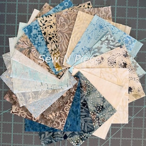May include: A collection of square fabric swatches arranged in a circular fan pattern, featuring various batik prints in shades of blue, beige, and brown. The fabric pieces display floral, dotted, and abstract patterns with the text Sew N Piece visible.