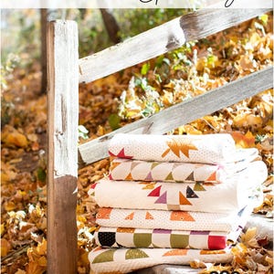 May include: A stack of folded quilts with autumn-themed patterns, including leaves and geometric shapes. The quilts are in shades of cream, orange, red, and green. The image includes the text "Pumpkin Spice Gatherings" and "Primitive Gatherings".