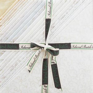 May include: A bundle of white fabric squares with a subtle pattern, tied together with a brown ribbon that reads "Island Batik".