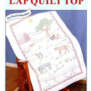 May include: A white lap quilt top with a cross-stitch and embroidery design featuring horses in a field. The quilt has a red border and includes a barn, tree, and fence. The text "LAP QUILT TOP" is displayed.