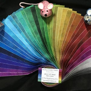 May include: A rainbow assortment of 40 fabric strips, each 2.5 inches wide, arranged in a fan shape. The fabric is 100% cotton and is part of the "Da Evolution" collection by In The Beginning fabrics. The label reads "(40) 2 1/2" Strips 100% Cotton In The Beginning Fabrics".