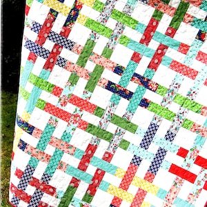 May include: A quilt pattern called "Basket Case" by Cluck Cluck Sew. The pattern is jelly roll friendly and is numbered #116. The quilt is made with a white background and colorful strips of fabric in red, green, blue, yellow, and pink.
