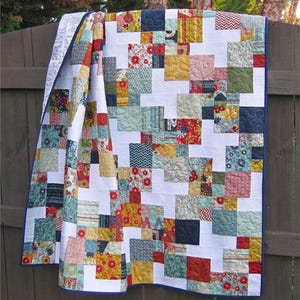 May include: A colorful quilt with a patchwork design, featuring squares of various patterns and colors, including red, blue, yellow, and green. The quilt is hanging on a wooden fence. The text "Peanut Butter Pinwheels" is at the top.