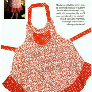 May include: A red and white patterned apron with a heart-shaped pocket and a ruffled hem. The apron has a button-on neck strap and is called "Sassy Little Apron".