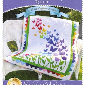 May include: A quilt pattern featuring a colorful butterfly design with a rainbow gradient and green flower stems. The quilt is displayed on a white wicker chair with a purple background. The text "Blooming Butterflies Quilt" and "Full-size diagrams included!" is displayed on the background. The text "Shabby Fabrics.com" is displayed at the bottom of the image.