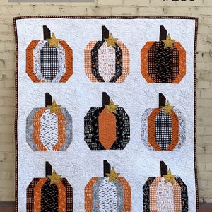 May include: A white quilt with nine orange, black, and white patchwork pumpkins. The quilt is titled "The Pumpkin Patch #250" and is from Cotton Street Commons.