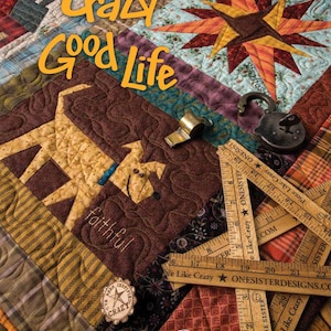 May include: A colorful quilt with the words "Crazy Good Life" in orange. The quilt features various fabric patterns, a star design, and a giraffe applique. Wooden rulers and a vintage lock are also visible.