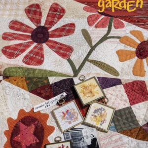 May include: A colorful quilt with large floral designs and the text "Stellar Garden." Several small, square, gold-framed pressed flower art pieces are displayed on the quilt, along with a vintage photograph.