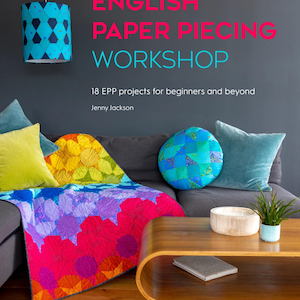 May include: A colorful living room scene featuring a sofa with decorative pillows and a vibrant quilt. The text "ENGLISH PAPER PIECING WORKSHOP" is displayed above the sofa. A wooden coffee table holds a bowl, a plant, and a book.