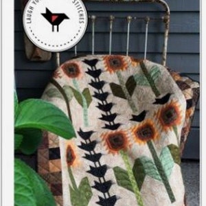 May include: A quilt with a sunflower and crow design. The quilt is 40 inches by 50 inches. The quilt is on a metal bed frame. The quilt is made with a variety of fabrics, including brown, green, and white. The quilt is called "And So It Crows".