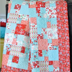 May include: A patchwork quilt featuring a variety of square fabric blocks in shades of red, light blue, and coral. The quilt displays patterns of birds, trees, and berries, with a border of red fabric printed with small berry clusters. Text reads Tidbits #SGD003 and Swirly Girls.