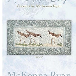 May include: A rectangular fabric quilt wall hanging titled At Water's Edge Classics by McKenna Ryan, measuring 30 inches by 16 inches. It features three sandpipers in brown and white tones standing on a sandy beach with green grass accents.