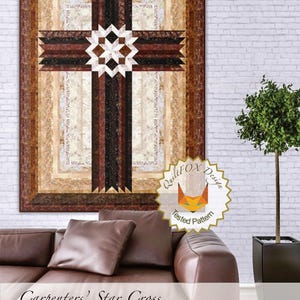 May include: A quilt pattern featuring a large brown cross with a star design in the center. The quilt is framed with a brown border and has a beige background. The quilt is 42 inches by 57 inches. The image also includes a brown leather couch and a potted plant.