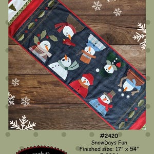 May include: A table runner featuring a winter theme with a row of snowmen in various poses and colors. The runner is made of fabric and has a red border. The text "SnowDays Fun" and "All Through the Night" are visible on the image. The finished size is 17 inches by 54 inches.