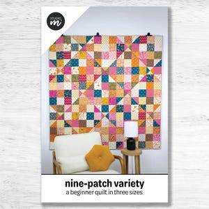 May include: A colorful nine-patch quilt in shades of pink, orange, teal, and yellow hangs on a wall. The quilt is made of square and triangular fabric patches. The image includes a white chair, a small table, and a lamp. The text reads "nine-patch variety".