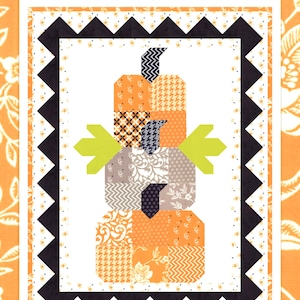 May include: A quilt pattern featuring a stack of three pumpkins made from patchwork fabric squares. The pumpkins are orange, gray, and black with a variety of patterns. The quilt is surrounded by a black and white border. The text "Pumpkin Trio" is at the top of the image. The text "Just a charm pack, a touch of green & some backgrounds...voila!" is at the bottom of the image. The text "FIG TREE & CO." is at the bottom of the image.