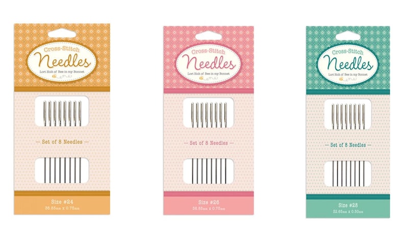Puede incluir: Tres paquetes de agujas de punto de cruz, cada uno con un fondo de color diferente: naranja, rosa y turquesa. Cada paquete contiene un juego de 8 agujas y est&aacute; etiquetado con el tama&ntilde;o de las agujas: #24, #20 y #28. El texto en los paquetes dice "Agujas de punto de cruz".