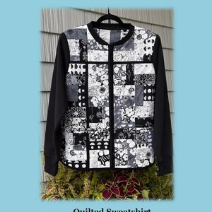 May include: A black and white quilted sweatshirt jacket featuring a patchwork design of various floral and geometric patterns. The jacket has a black collar, black sleeves, and a front zipper closure. The text JMD-202 Charm Pack Quilted Sweatshirt Jacket is visible.