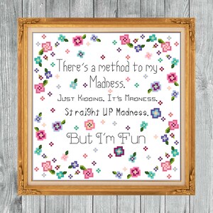 May include: A framed cross-stitch artwork with a gold-colored ornate frame. The artwork features the text "There's a method to my Madness. Just Kidding. It's Madness. Straight UP Madness. But I'm Fun" surrounded by floral pixel art.