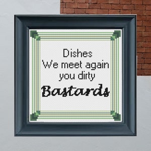 Könnte beinhalten: Gerahmte Kreuzstichkunst mit einem dunkelblauen Rahmen. Das Kunstwerk zeigt den Text "Dishes, We meet again you dirty Bastards" in Schwarz und Grün auf weißem Hintergrund. Der Hintergrund ist eine Backsteinmauer.