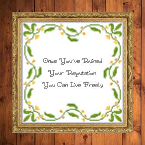 May include: A framed cross-stitch artwork with a gold-colored ornate frame. The artwork features the text "Once You've Ruined Your Reputation You Can Live Freely" surrounded by a green and yellow floral border.